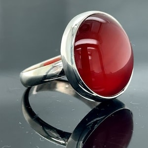 May include: A silver ring with a large, round, red carnelian gemstone. The ring is set in a simple, elegant style.