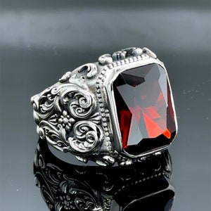 May include: A silver ring with an ornate design and a large, red, faceted gemstone.