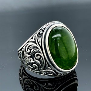 May include: A silver ring with an ornate design and a large oval green gemstone.