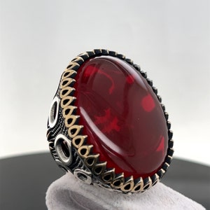 May include: A silver ring with a large, oval-shaped red gemstone set in a detailed silver and gold band.