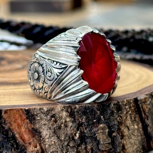 Puede incluir: Un anillo de plata con un diseño ornamentado y una gran piedra ovalada roja.