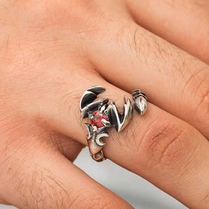 Peut inclure: Une bague en argent en forme de scorpion avec une pierre précieuse rouge au centre. La bague est portée au doigt.
