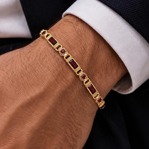 Può includere: Un bracciale in oro caratterizzato da un motivo ripetitivo di rubini rossi rettangolari taglio baguette e piccoli rubini rossi rotondi incastonati in maglie di metallo dorato decorate. Il design alterna le pietre rettangolari e rotonde.
