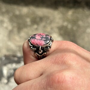 May include: A silver ring with a pink and black gemstone set in a detailed design.