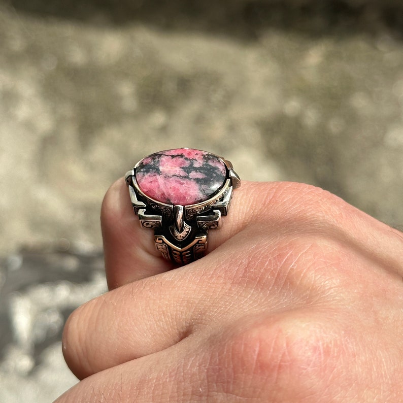 May include: A silver ring with a pink and black gemstone set in a detailed design.