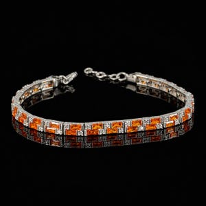 May include: A silver-toned bracelet featuring a double row of rectangular orange gemstones alternating with small clear stones. The bracelet has a metallic link chain construction with a clasp mechanism visible at one end of the jewelry piece.
