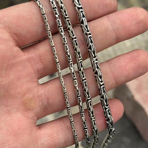 May include: Four silver chain necklaces of varying lengths and widths. The chains are all made of a tightly woven, box-style design.