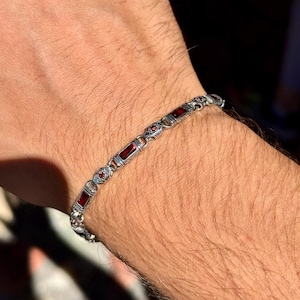 May include: Silver bracelet with rectangular red gemstones and ornate detailing. The bracelet is composed of interconnected links, with each link featuring a red stone. The design includes small, round red accents between the larger stones.