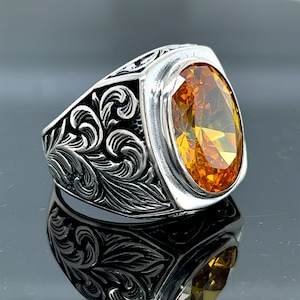 May include: A silver ring with an ornate floral design and a large, oval-shaped amber gemstone.