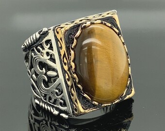 May include: A silver and gold ring with a large oval tiger's eye gemstone set in a detailed ornate design.