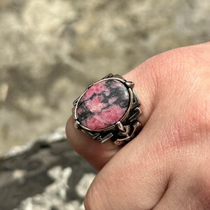 May include: A silver ring with a pink and black gemstone set in a detailed design.
