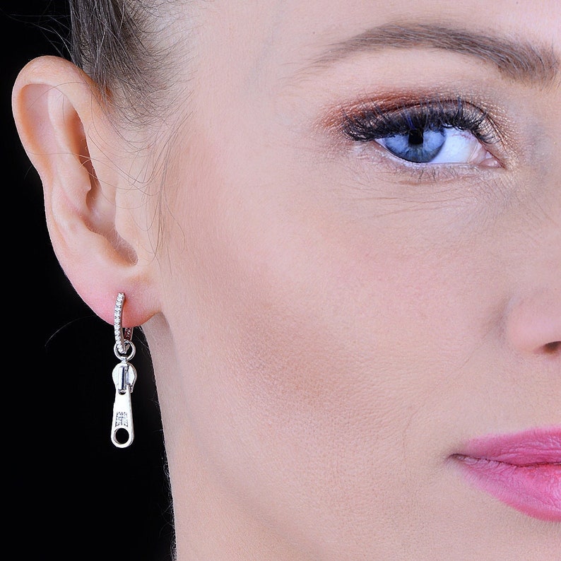 May include: Silver zipper charm earrings with a small hoop and clear cubic zirconia stones.