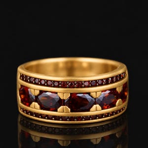 Könnte beinhalten: Ein breiter Goldring mit einer mittleren Reihe aus oval geschliffenen, tiefroten Granat-Edelsteinen, die durch Goldstege getrennt sind, flankiert von zwei schmaleren Reihen aus kleinen, rund geschliffenen roten Granaten an den Rändern.