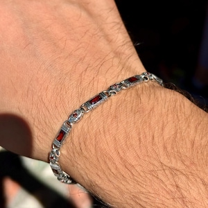 May include: Silver bracelet with rectangular and round red gemstones. The bracelet is made of silver and features an ornate design. The gemstones are a deep red color, and the bracelet is worn on a wrist.
