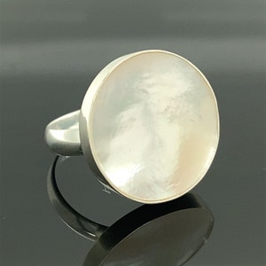 Puede incluir: Un anillo de plata con una piedra grande, redonda y blanca de nácar.