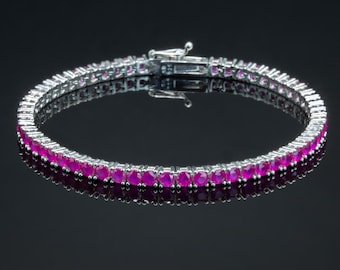 Peut inclure: Un bracelet de tennis argenté orné d'une rangée de pierres précieuses roses vives. Le bracelet est présenté sur un fond sombre, soulignant l'éclat des pierres et le fermoir en métal poli.