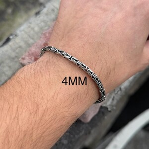 May include: A silver chain bracelet with a 4mm width. The bracelet is shown on a person's wrist.
