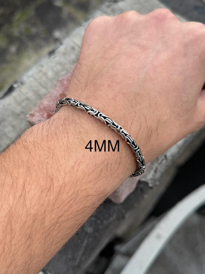 May include: A silver chain bracelet with a 4mm width. The bracelet is shown on a person's wrist.