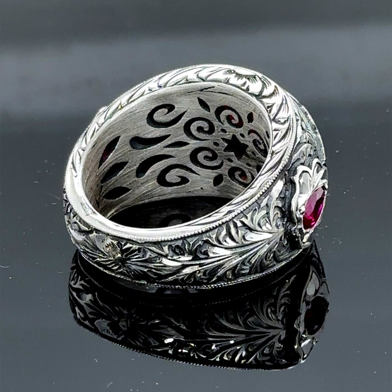 Peut inclure: Une bague en argent avec des gravures florales complexes et une seule pierre pr&eacute;cieuse rouge sertie dans la bande.