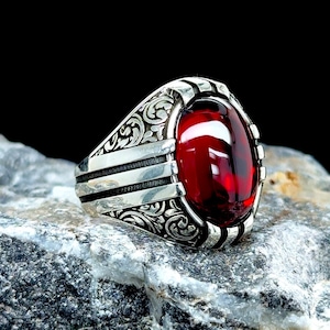Puede incluir: Un anillo de plata con un diseño adornado y una gran piedra roja de forma ovalada.