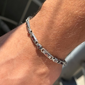 May include: Silver bracelet with rectangular red gemstone accents. The bracelet features ornate detailing and is worn on a wrist. The design incorporates small, round red stones and decorative metalwork, creating a classic look.