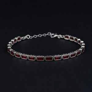 May include: A silver bracelet with rectangular, deep red gemstones set in a row. The bracelet has a delicate chain and clasp. The gemstones are evenly spaced and create a striking contrast against the silver setting.