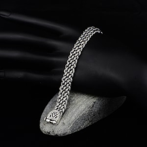 May include: A silver chain bracelet with a detailed clasp. The bracelet is made of a braided chain design.