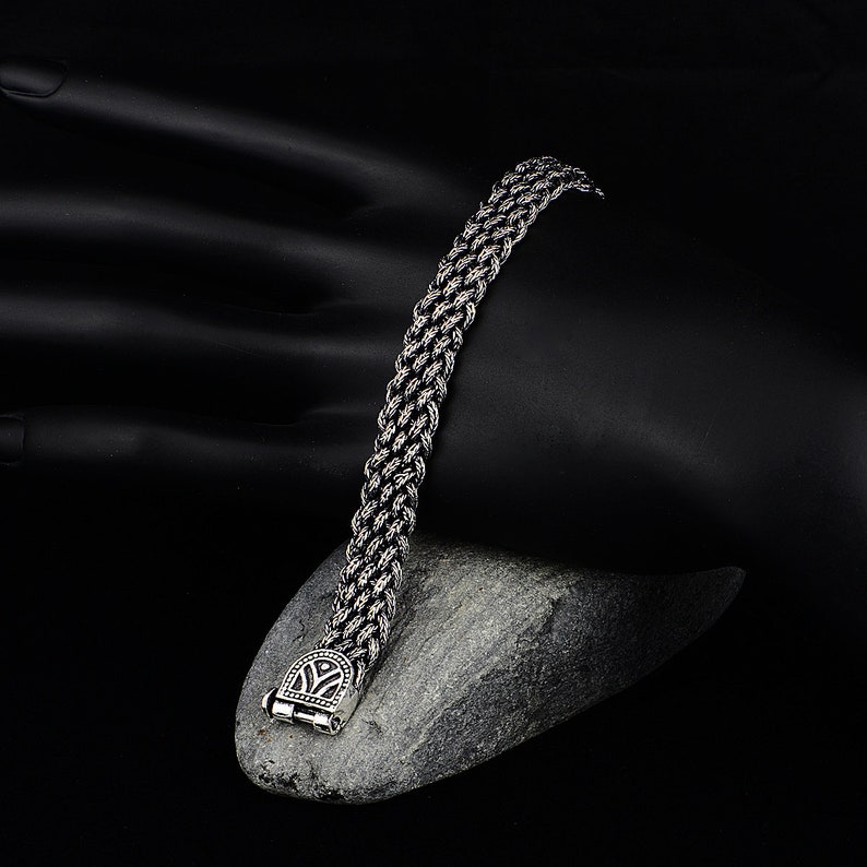 May include: A silver chain bracelet with a detailed clasp. The bracelet is made of a braided chain design.
