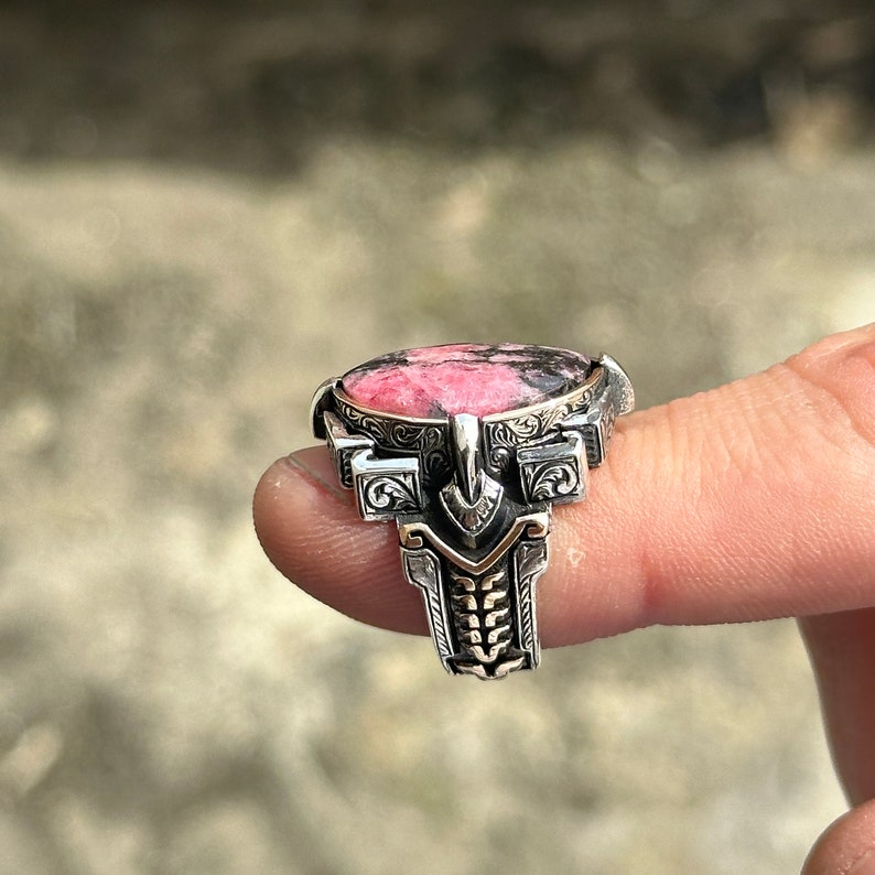May include: A silver ring with a pink and black gemstone set in a detailed, ornate design.