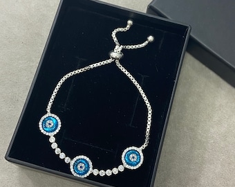 May include: A silver bracelet with three blue evil eye charms. The bracelet is adjustable and has a delicate chain.