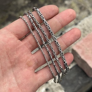 May include: Four silver chain necklaces of varying widths, displayed on a hand.
