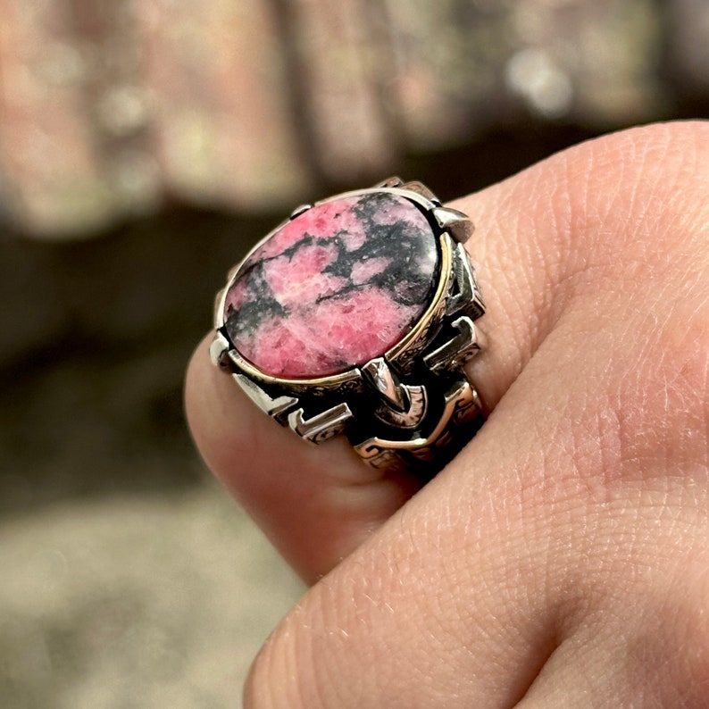May include: A silver ring with a pink and black gemstone set in a detailed silver and gold setting.