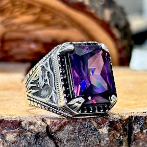 May include: A silver ring with an ornate design and a large, faceted, purple gemstone.