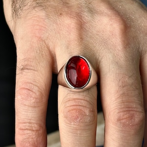 May include: A silver ring with a large, oval-shaped, red gemstone.
