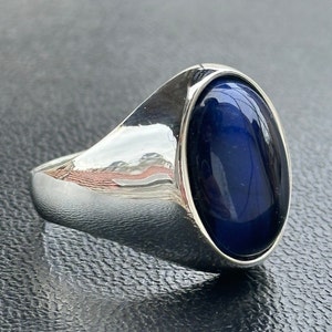 May include: A silver ring with a large oval blue gemstone. The ring has a smooth, polished finish.
