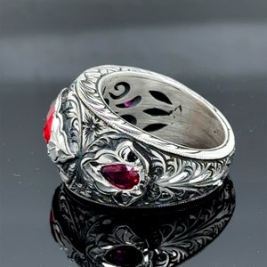 Peut inclure: Une bague en argent avec des sculptures florales complexes et deux pierres pr&eacute;cieuses rouges. La bague est con&ccedil;ue avec une large bande et un design d&eacute;taill&eacute;.