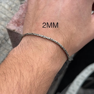 May include: A silver chain bracelet on a person's wrist. The chain is 2mm wide.