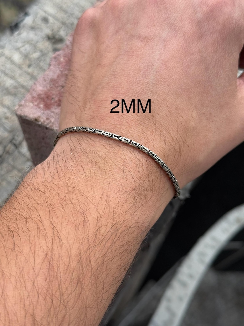 May include: A silver chain bracelet on a person's wrist. The chain is 2mm wide.
