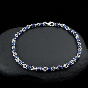 May include: A silver bracelet with rectangular blue gemstones. The bracelet is composed of alternating silver links and blue gemstones, creating a continuous chain. The clasp is a simple hook and eye closure.