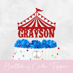 May include: Red glitter circus tent cake topper with the name Grayson in red glitter. The topper is on a white cake with blue frosting and red and blue sprinkles.