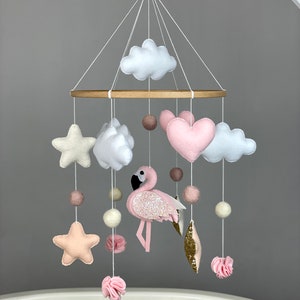 May include: A pink and white baby mobile with a pink flamingo, clouds, stars, and hearts hanging from a wooden ring.