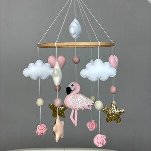 May include: A pink and white baby mobile with a pink flamingo, clouds, stars, and hearts. The mobile is hanging from a wooden ring.
