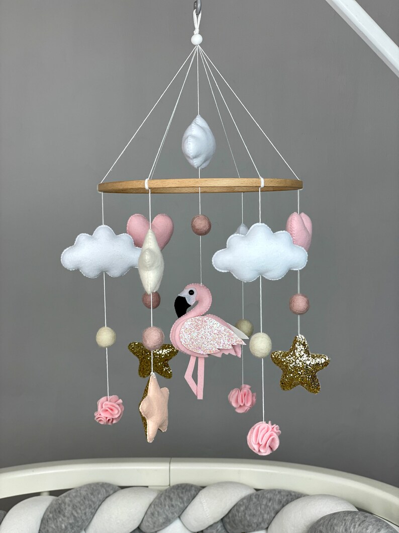 May include: A pink and white baby mobile with a pink flamingo, clouds, stars, and hearts. The mobile is hanging from a wooden ring.