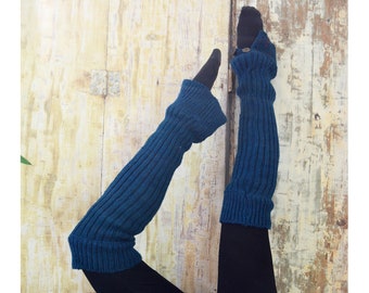 May include: A pair of teal blue knitted leg warmers with a button detail. The leg warmers are worn on a person's legs, with the feet and lower legs covered in black pants.