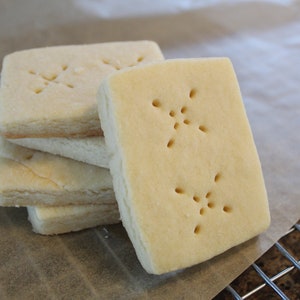 May include: A stack of four plain shortbread cookies with a decorative pattern of small holes on the top. The cookies are on a piece of parchment paper.