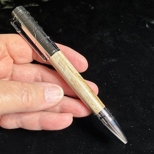 May include: A ballpoint pen featuring a light-colored, natural wood grain barrel and polished chrome metal components. The pen cap includes a metal clip and is engraved with the text "WHEN YOU ONLY HAVE A HAMMER, EVERYTHING LOOKS LIKE A NAIL."