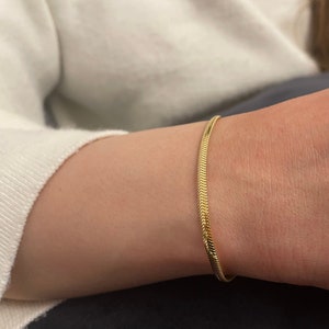 May include: A gold snake chain bracelet on a person's wrist.