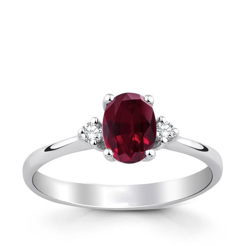 May include: A silver ring with a large oval-shaped ruby gemstone and two smaller diamond accents.