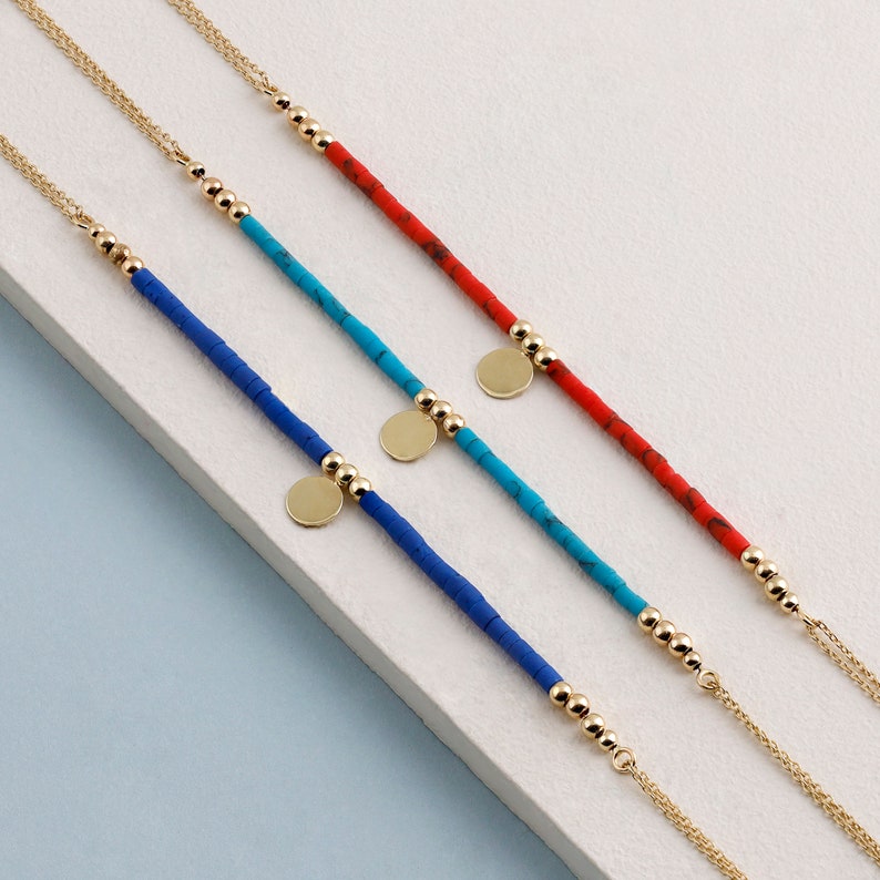 May include: Three gold chain bracelets with colorful beads and gold disc charms. The bracelets are layered on a white surface.