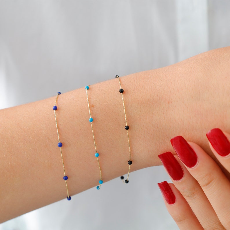 May include: Three gold chain bracelets with small beads. The bracelets have blue, turquoise, and black beads.